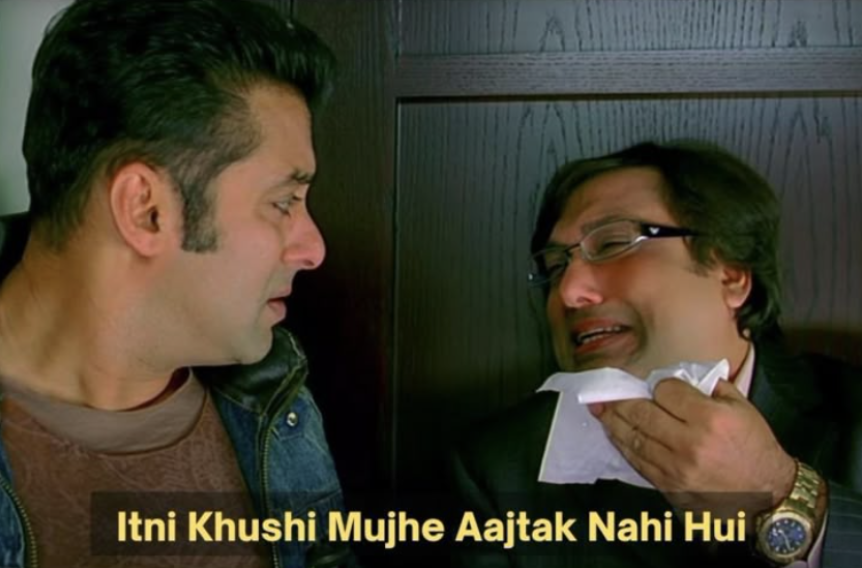 Movie still meme of two men: one in a denim jacket looks on while the other, in glasses and a suit, dabs his teary face with a tissue. Caption: “Itni Khushi Mujhe Aajtak Nahi Hui” (I have never been this happy)